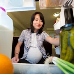 A pregnant woman reaching for a jar of pickles inside a refrigerator, Should You Refrigerate Pickles? [And For How Long?]