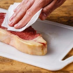 A raw meat steak drying up excess moisture with paper towel, How To Pat Dry Chicken Or Meat [Inc. Without Paper Towels]
