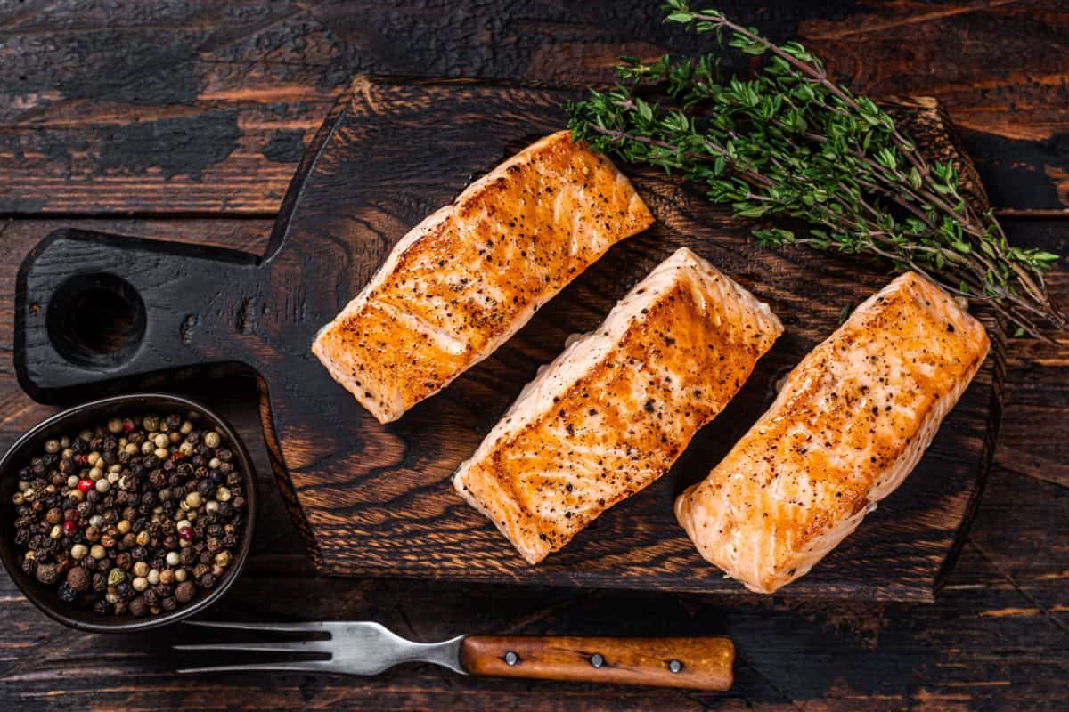 Slices of baked salmon on a chopping board with thyme on the side
