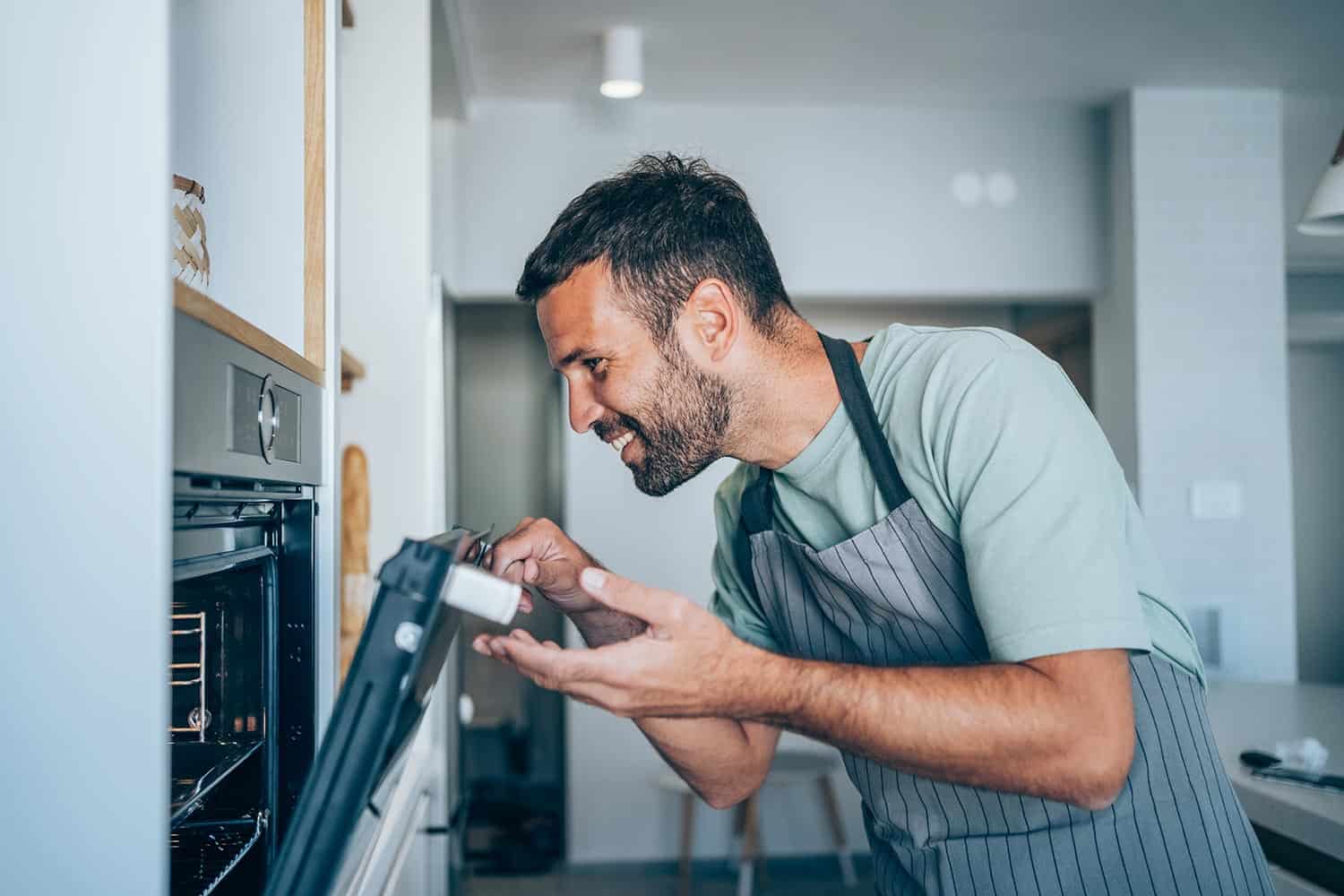 Smiling man checking food in the oven