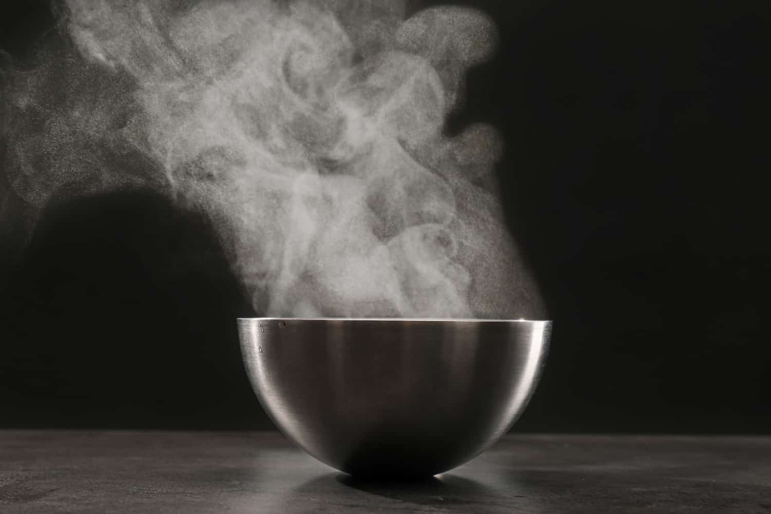 Steaming metal bowl on grey table against dark background