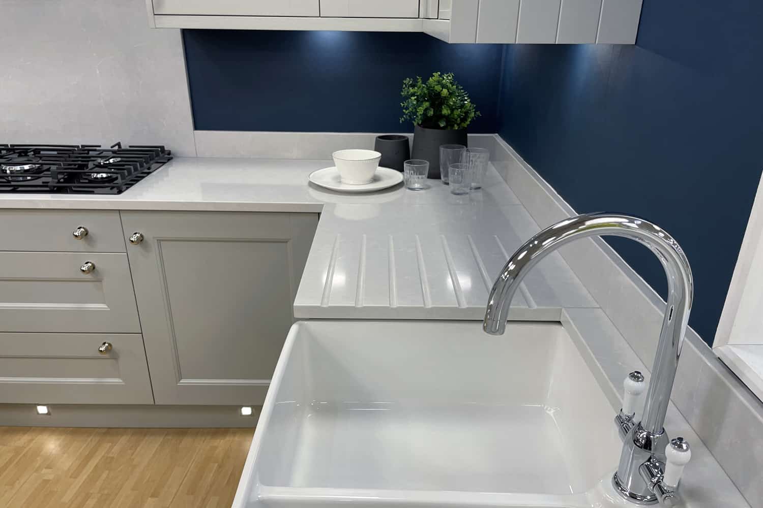 Stock photo showing a ceramic, double kitchen butler sink and white stone, corian kitchen counter with integrated grooved granite draining board.