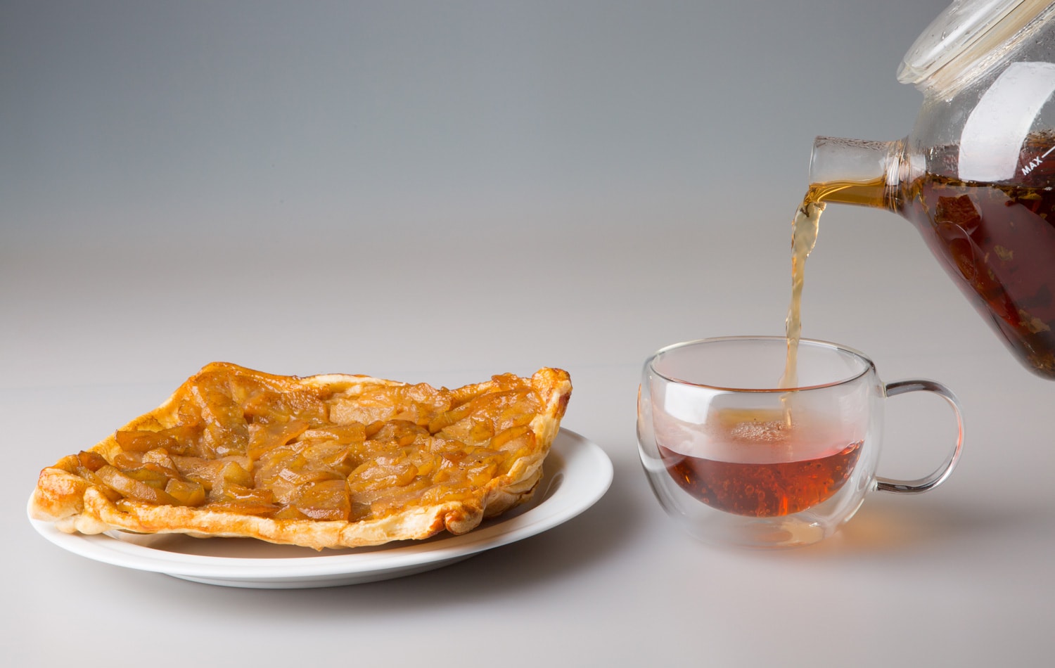 Tea drinking. A piece of pear pie in a saucer and a transparent double-walled cup. Freshly brewed black tea is poured from a teapot into a cup. stock photo
