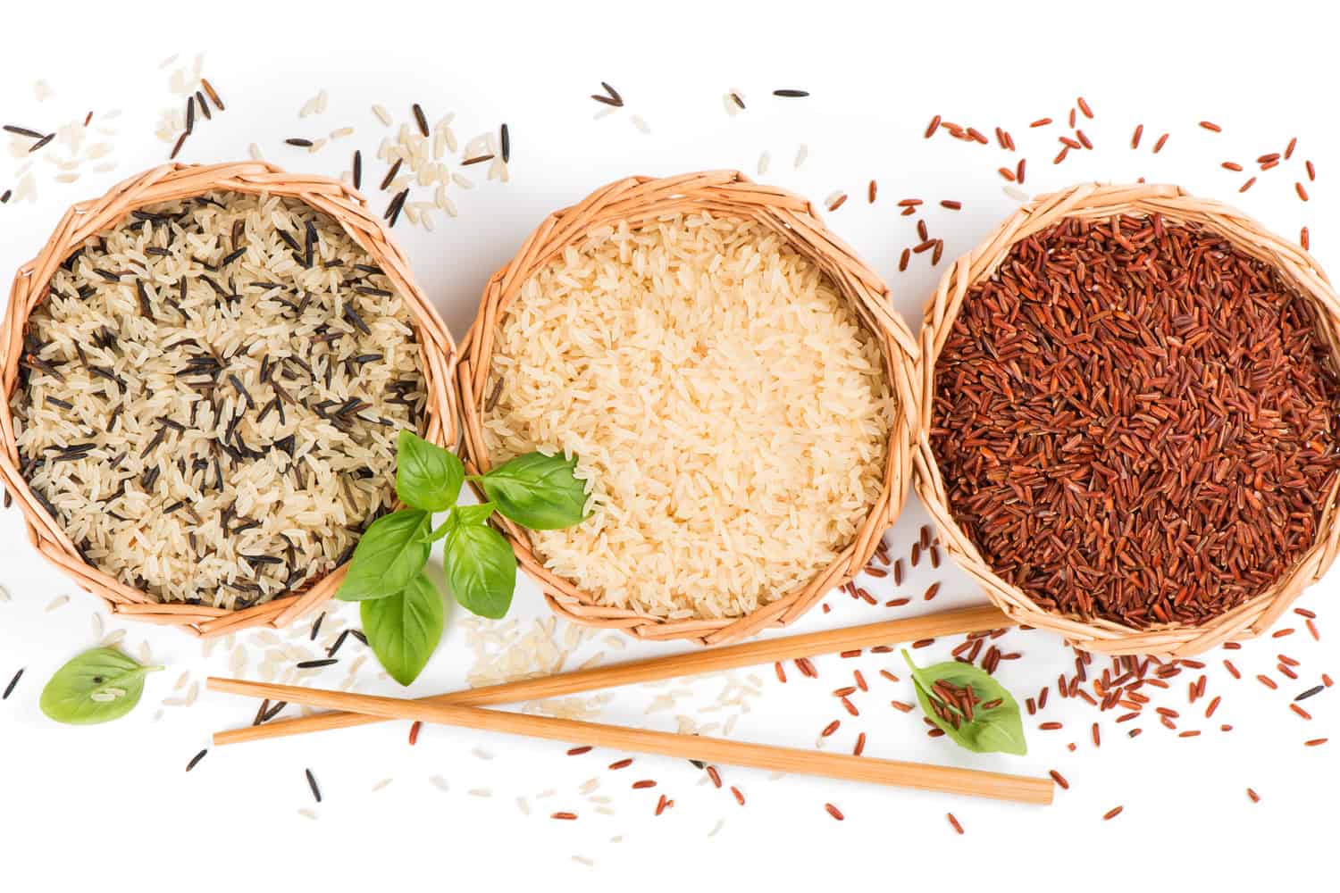 Top view of different rice types in a baskets decorated with basil and chopsticks isolated on white background