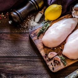 A top view of two chicken breasts on a cutting board surrounded by various ingredients for seasoning, How To Make Seasoning Stick To Chicken