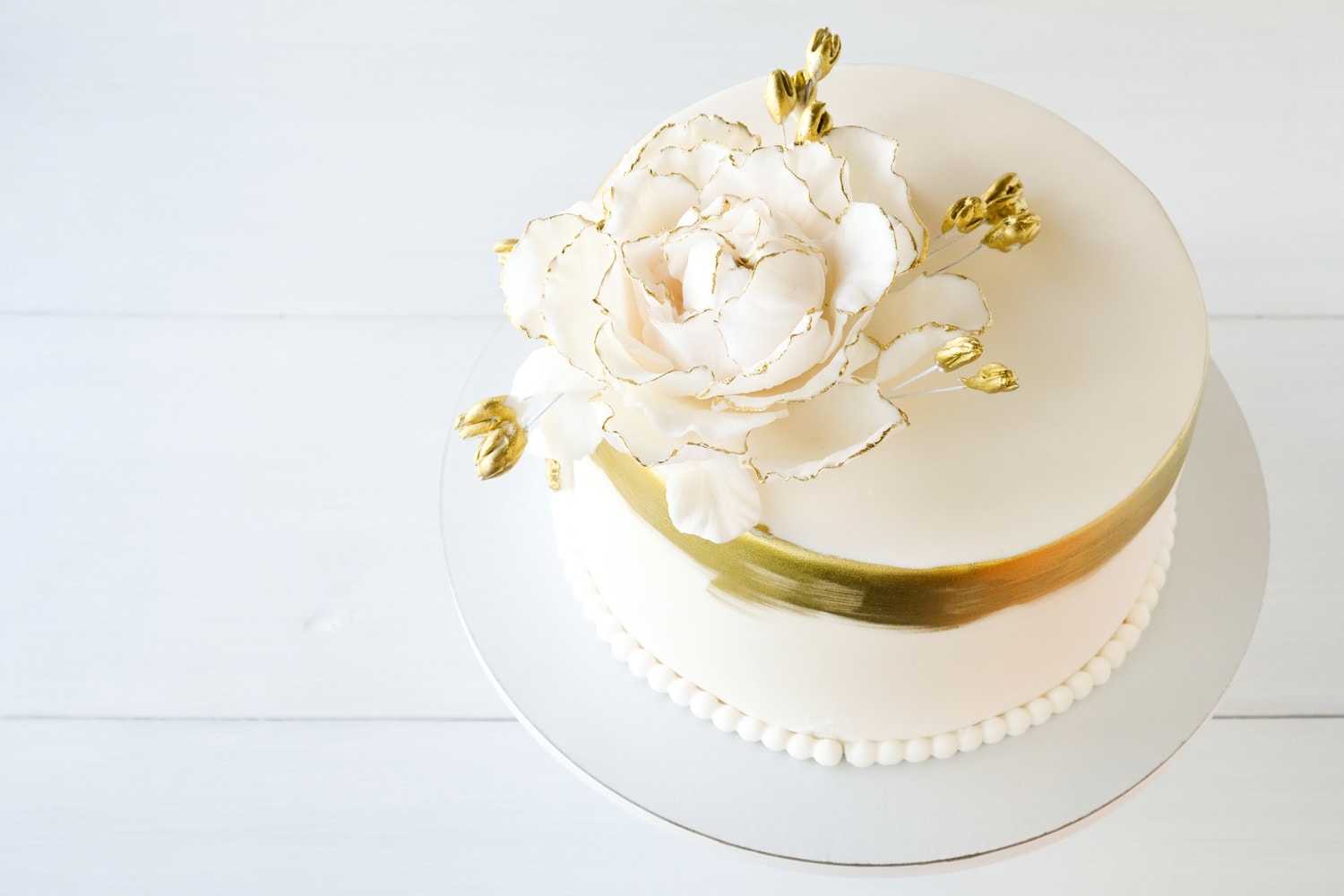 White wedding cake decorated with gold flowers on a white background.