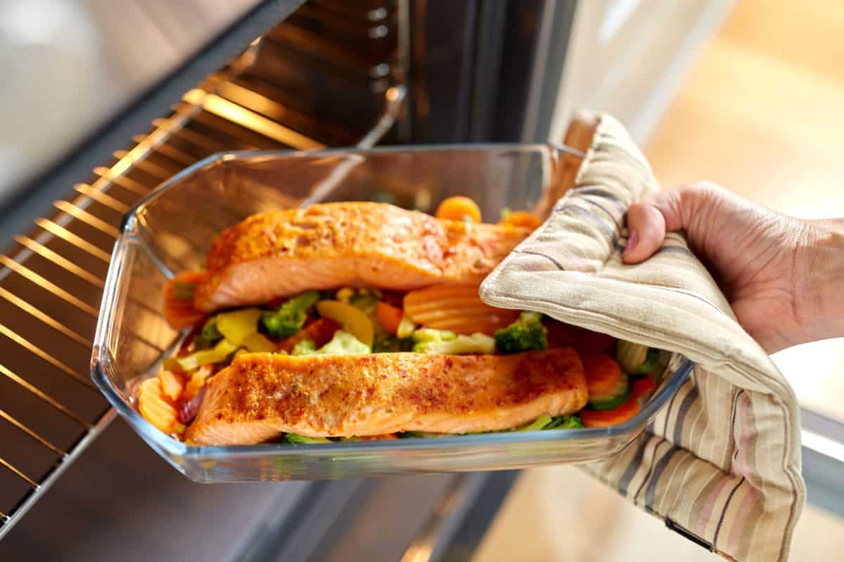 Woman baking salmon with broccoli, carrots and other spices