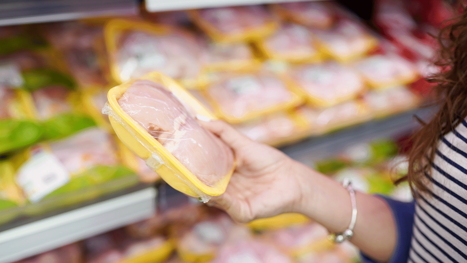 Woman choosing packed fresh chicken meat in supermarket