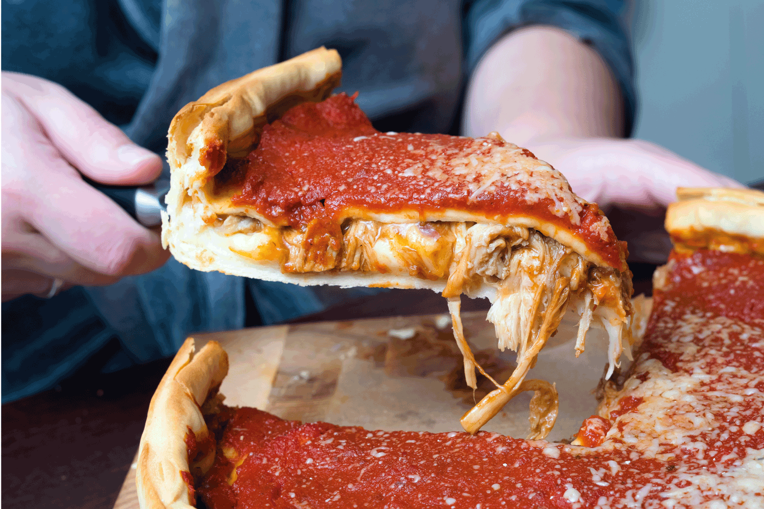 Woman hands cutting Chicago style deep dish Italian cheese pizza with tomato sauce and beef meet inside