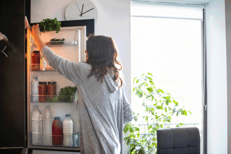 Woman holding the fridge door and taking a bunch of parsley, Fridge Not Cooling But Light Is On - What To Do?