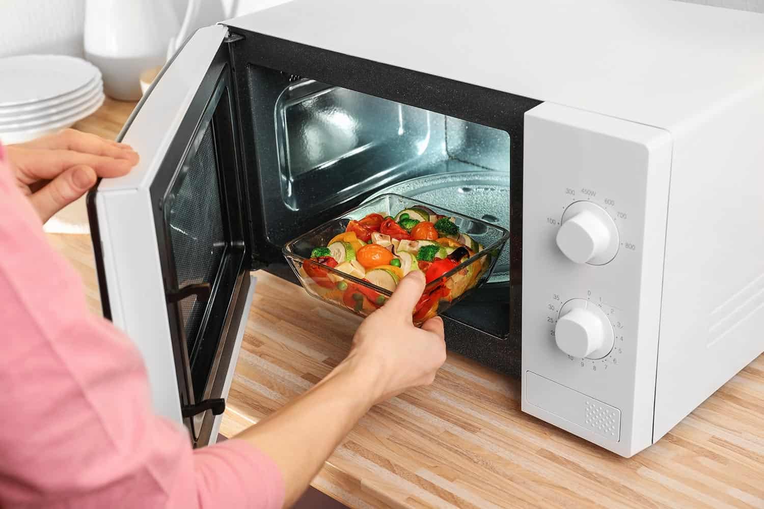 Woman putting bowl with vegetables in microwave oven