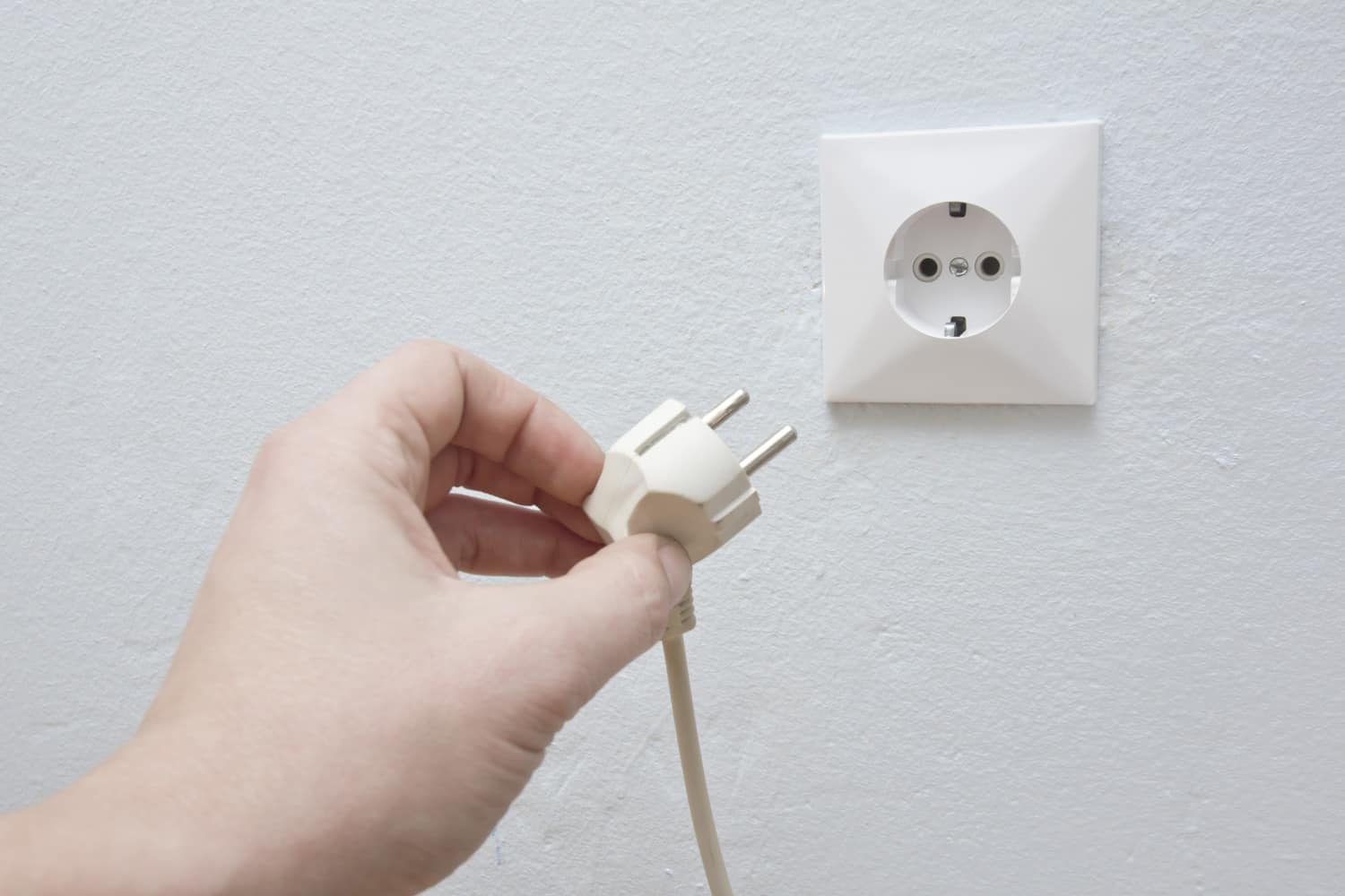 hand holding power cable in front of wall outlet