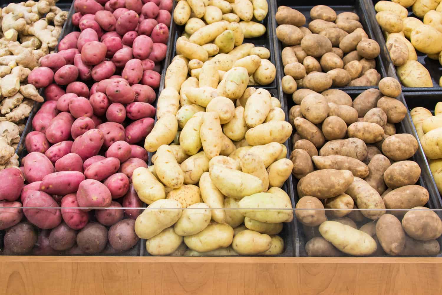 Grocery store displays different colors and varieties of potatoes for people to select thei favourite agricultural produce arranged in lines