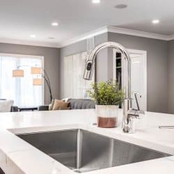 A kitchen sink in a luxurious home looking out towards a living room area, How to Tighten A Loose Kitchen Faucet Base
