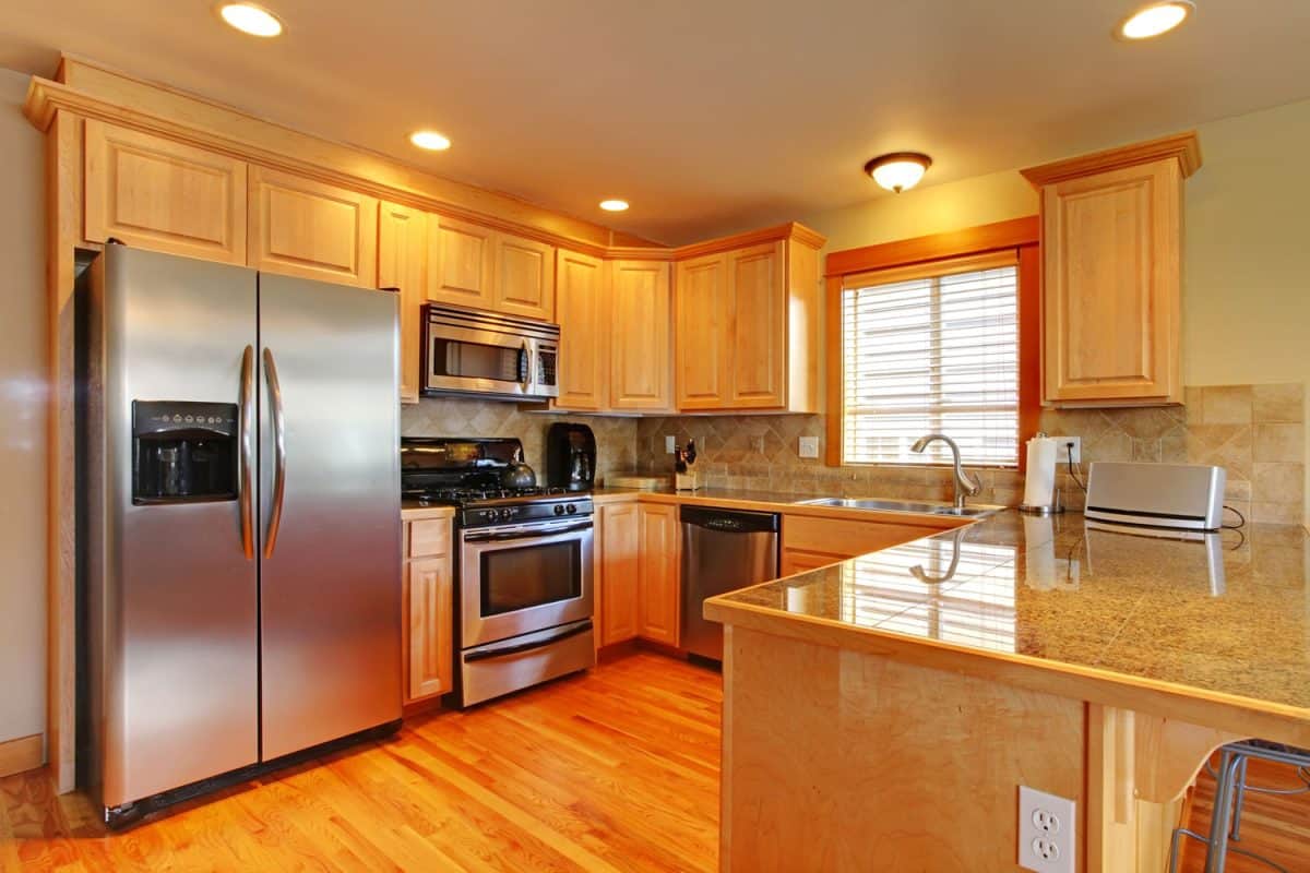 A spacious and luxurious kitchen with wooden flooring, maple cabinets and cupboardswith stainless steel kitchen appliance