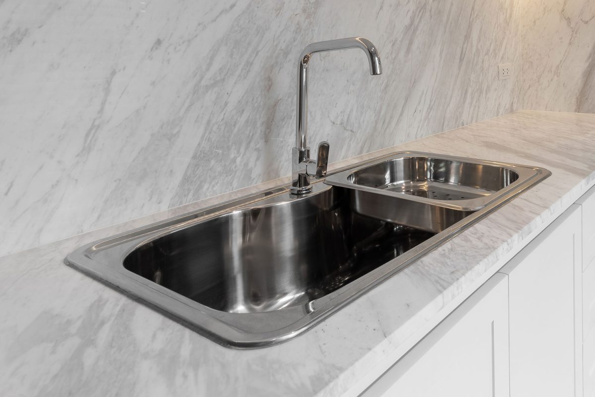 A stainless steel modern drop in kitchen sink with white marble countertop