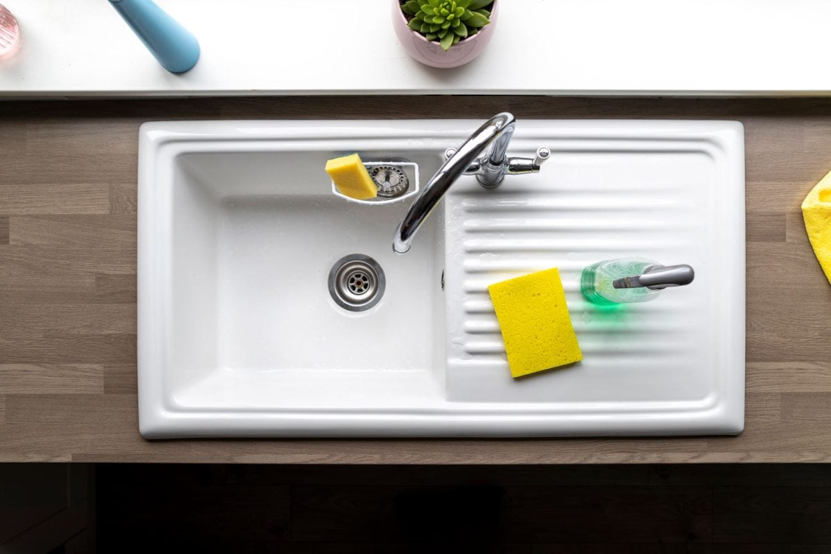 A white coated single sink with a flat area with sponges and dishwashing liquids