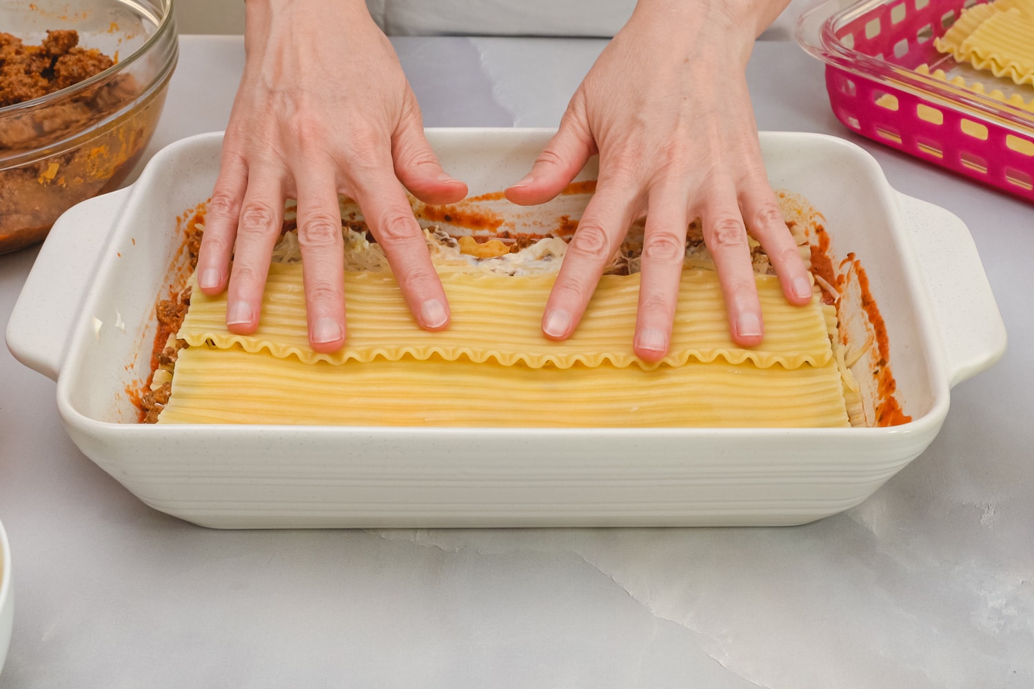 Beef lasagna step by step recipe. Layer of lasagna noodles. Close up front view, woman hands, marble kitchen table background