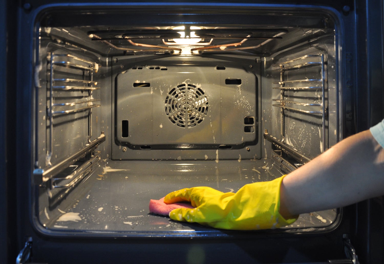 Cleaning the oven in the kitchen. hand in a yellow household glove out of focus on the background of the oven.
