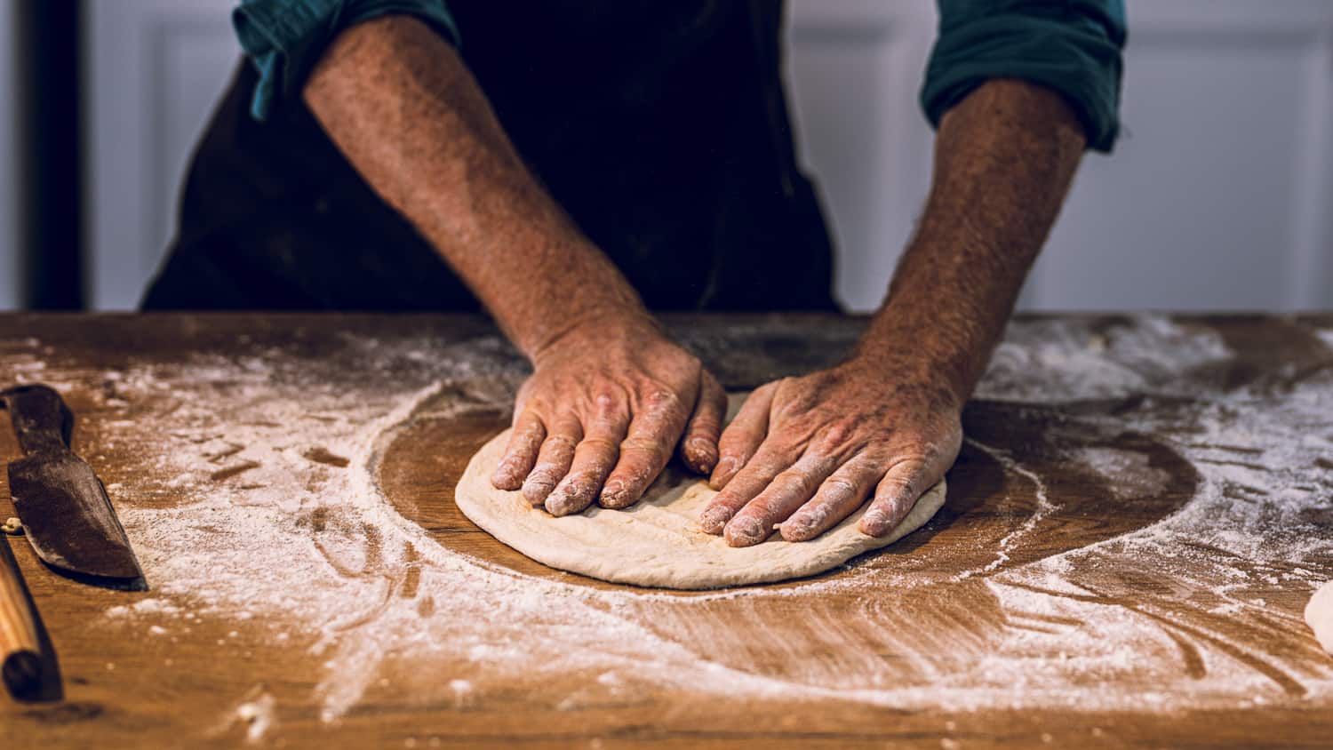 Close-up of chef's hands kneading pizza dough in kitchen.