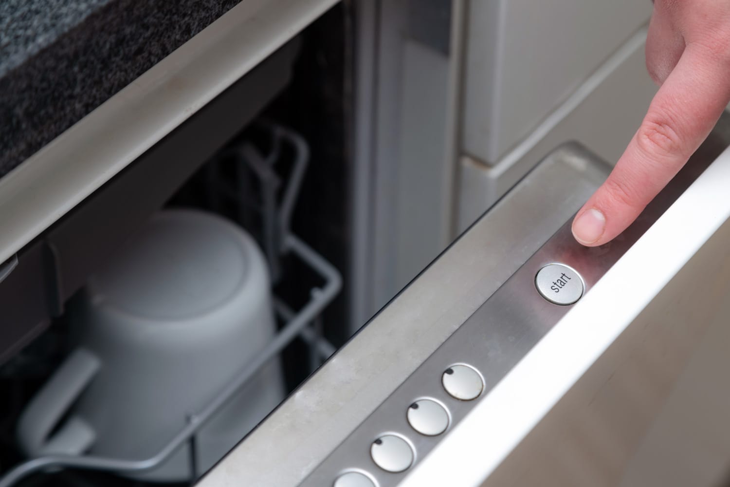 Close up of finger pressing start button on dishwasher in the kitchen. Hand starting dish washer machine