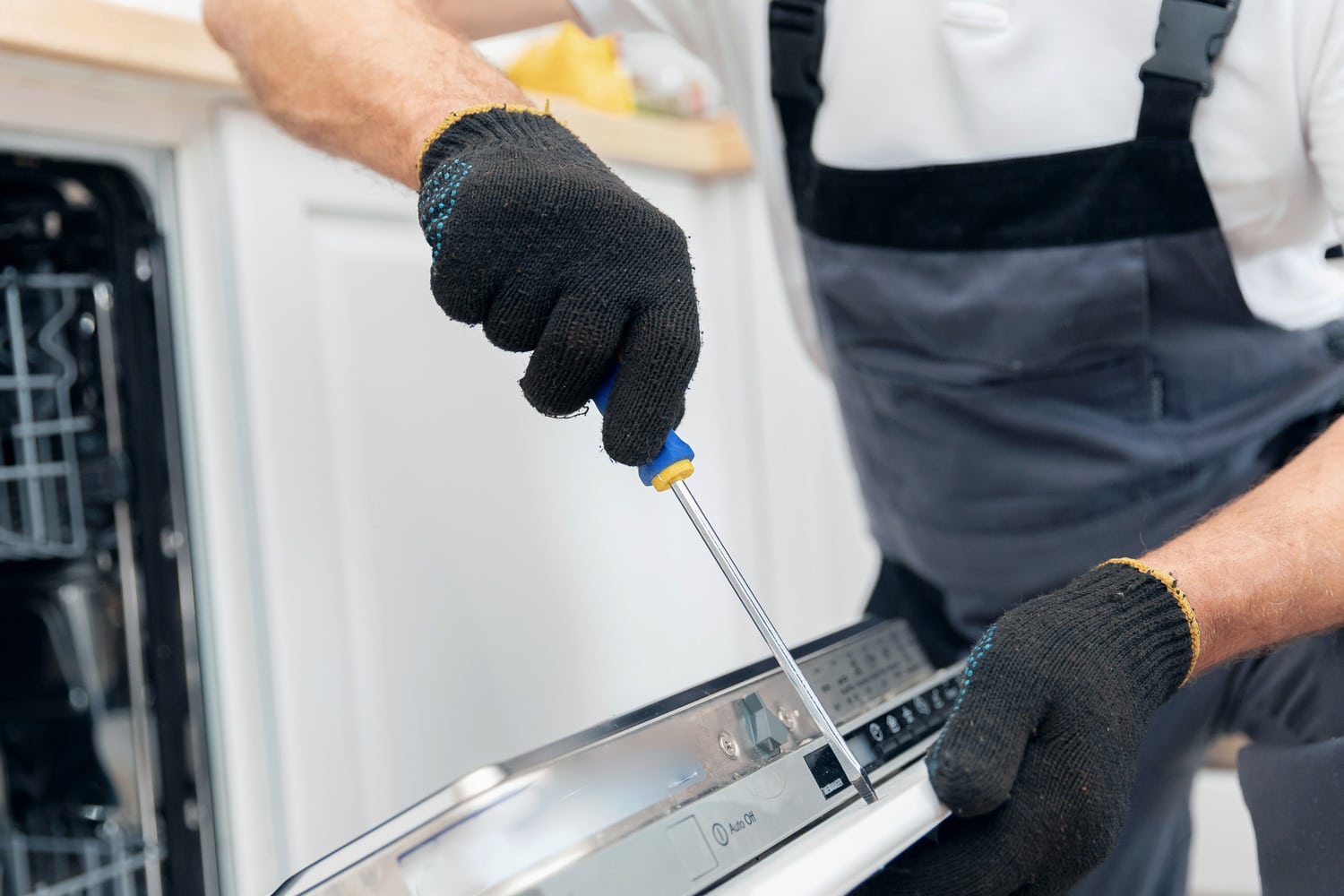 Closeup repair and installation of dishwasher, male worker with tool in uniform.