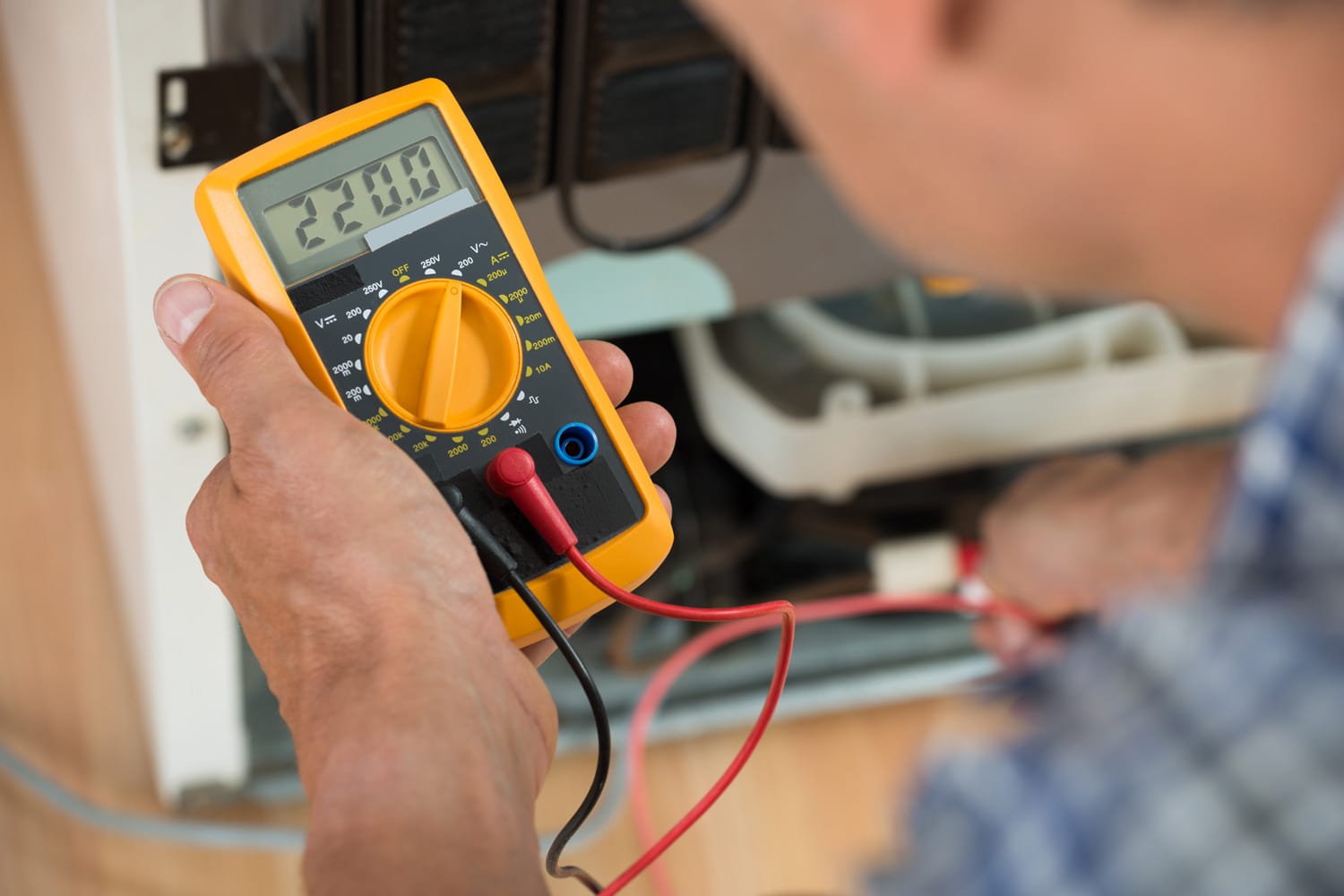 Cropped image of male repairman checking fridge with digital multimeter at home