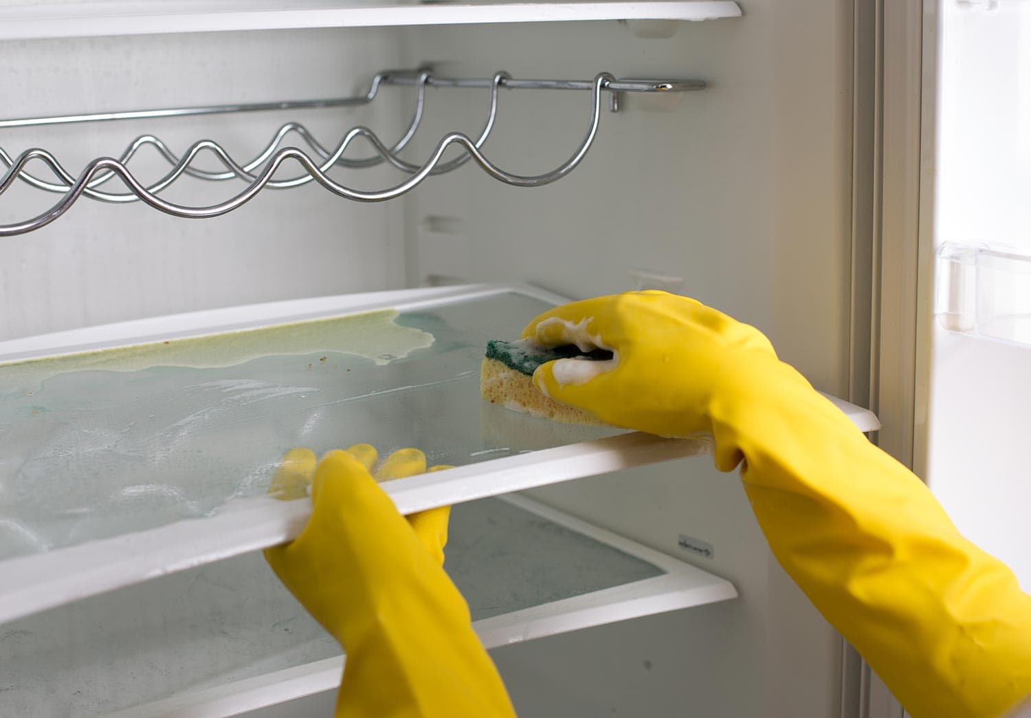 Female hands with protective gloves cleaning empty refrigerator