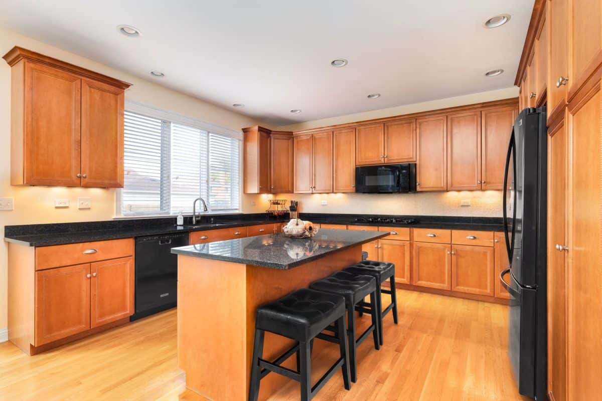 Luxurious and spacious kitchen with maple cabinets and cupboards with a matching black countertop on the breakfast bar and main kitchen area