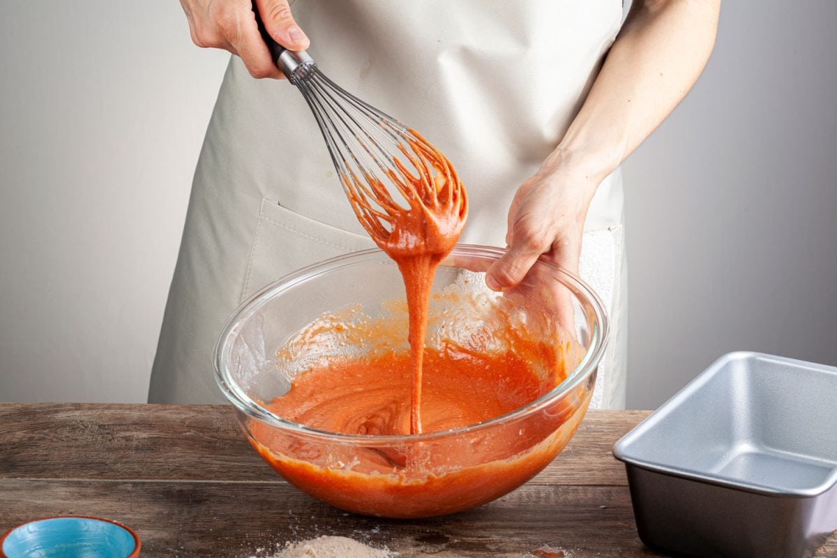 Man mixing orange food coloring in a glass mixing bowl