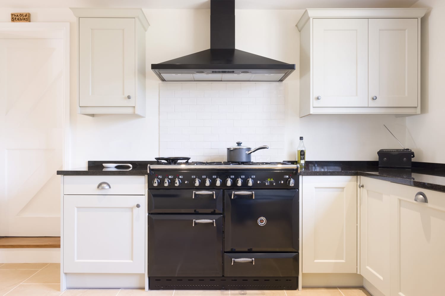 Modern modular kitchen interior in black and off white, with range cooker and chimney extractor hood.