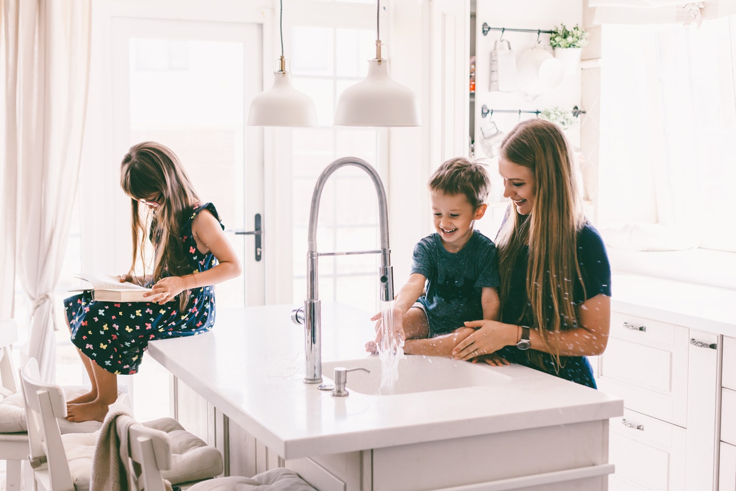 Mother with her children playing with water in kitchen sink at home. Happy lifestyle family moments.