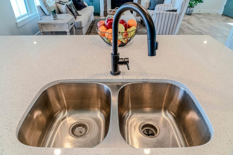 Stainless steel sink with two bowls and black curved faucet against fruit basket - How To Unclog A Double Kitchen Sink Without A Garbage Disposal