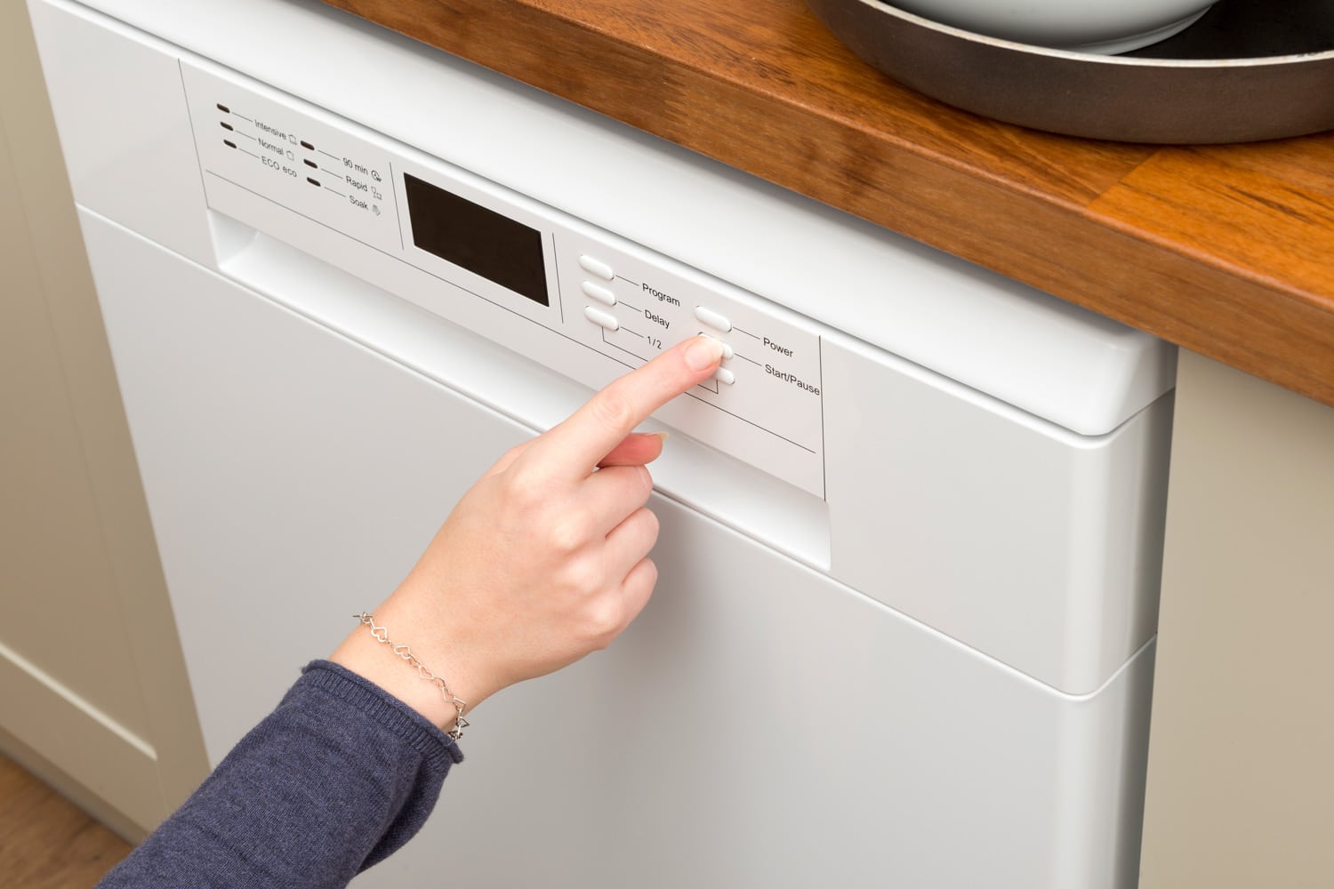 Woman's finger pressing the 'start' button of a dishwasher