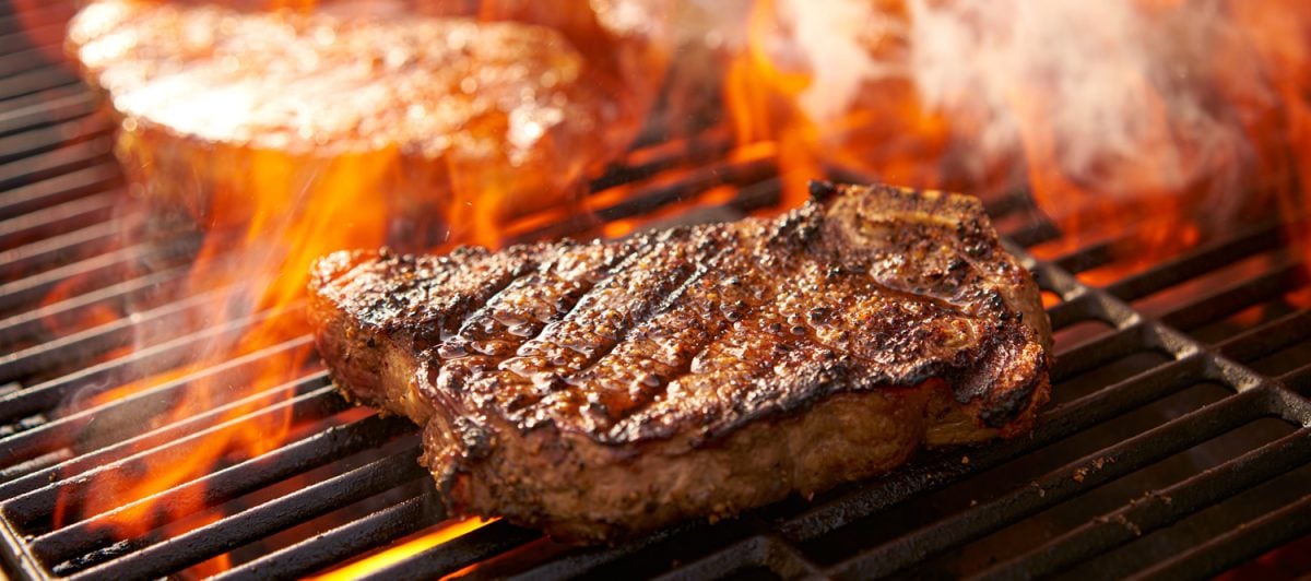 rib-eye steaks cooking on flaming grill