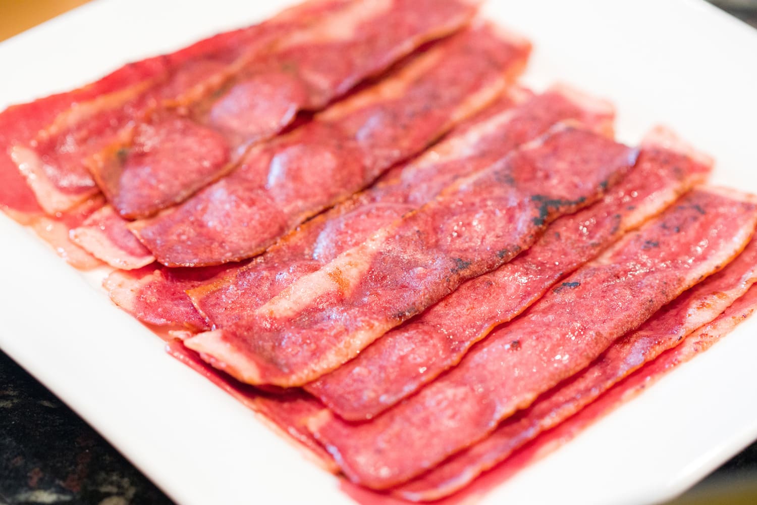 A close up photograph of several sizzling hot turkey bacon slices or pieces on a white serving plate on a kitchen counter ready to eat for breakfast.