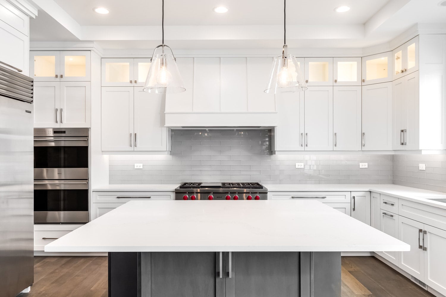 A luxurious modern kitchen with stainless steel Wolf appliances surrounded by white cabinets, beautiful granite, and hardwood floors.