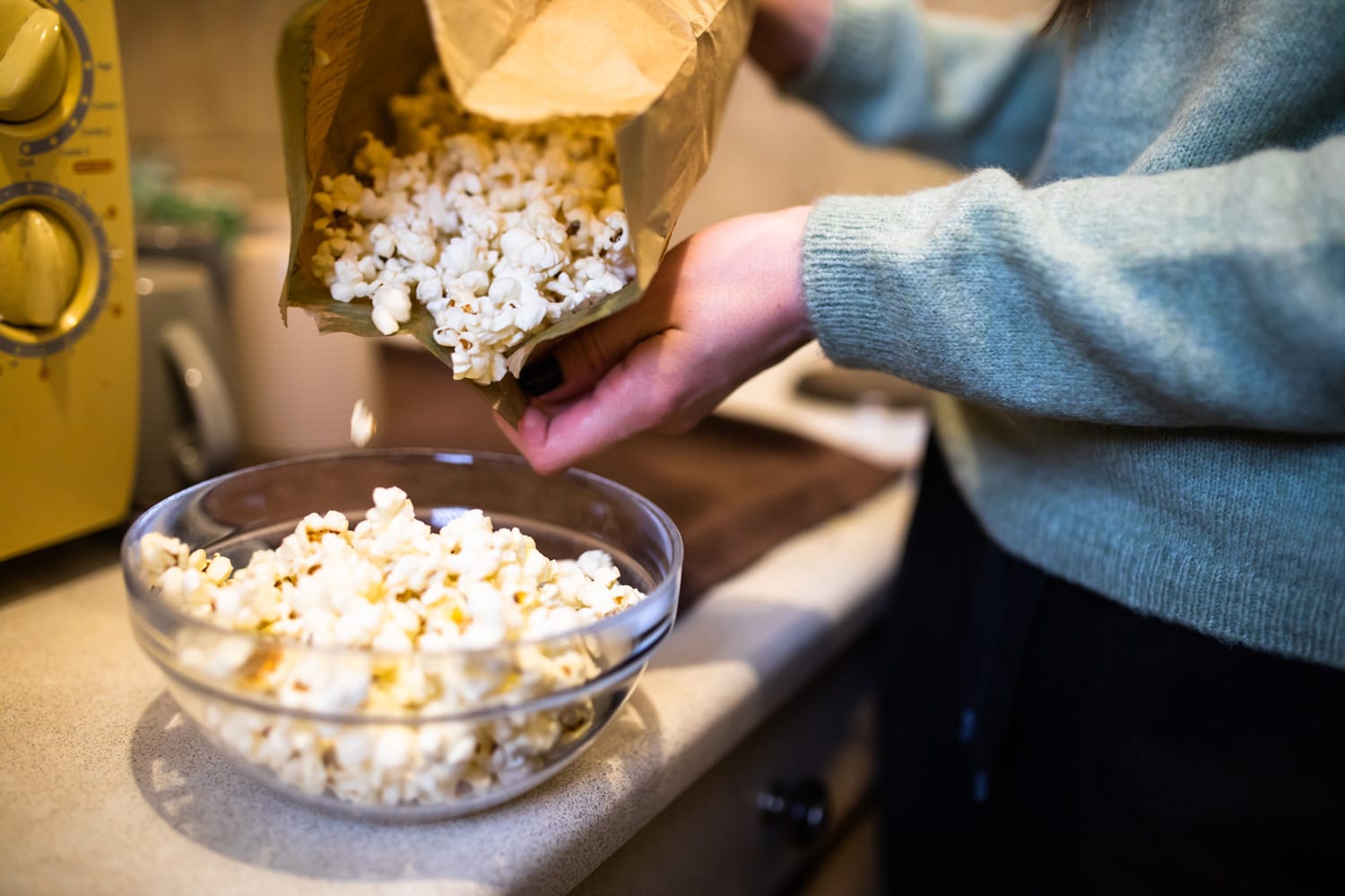 A cropped shot of a young woman pouring microwave popcorn from the bag into a bowl