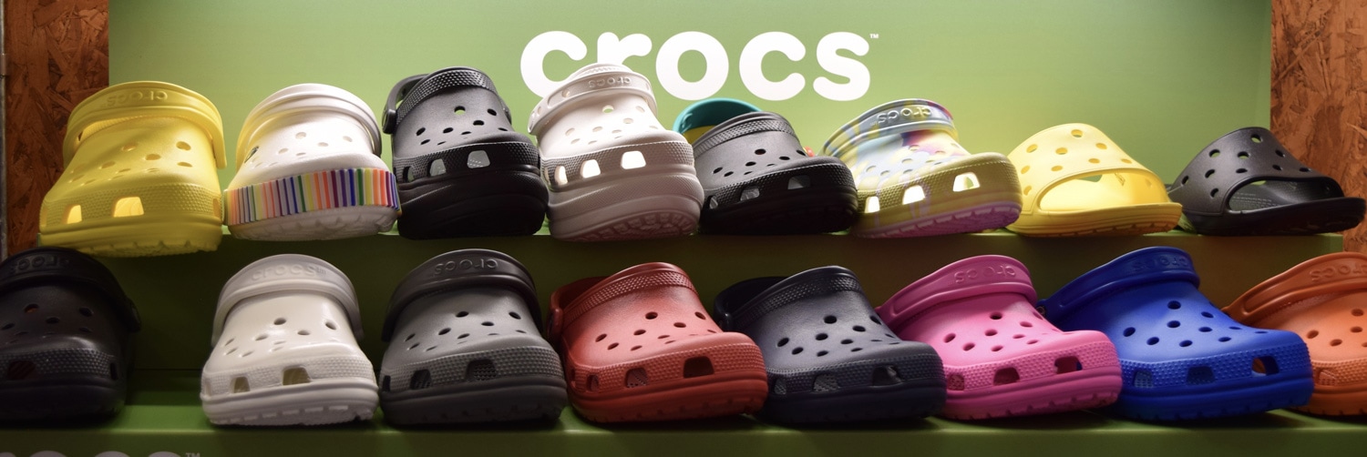 A photo bright different colors of Croc Shoes on store shelf with CROCS in white on green background