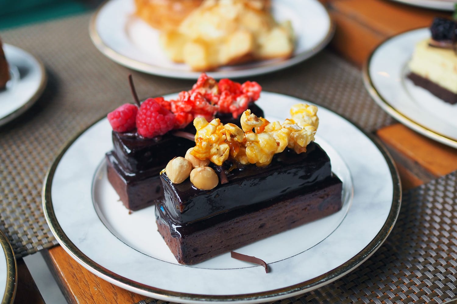 A plate of delicious homemade dark chocolate cake; topped with caramel popcorn and nuts, and strawberry popcorn and raspberry