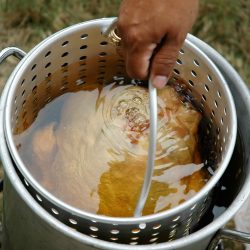 A turkey slowly gets lowered into a large pot of hot peanut oil for frying - How Long to Fry a Turkey? [Per Pound]