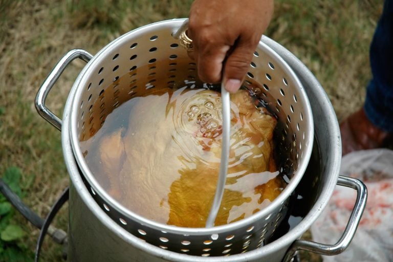 A turkey slowly gets lowered into a large pot of hot peanut oil for frying - How Long to Fry a Turkey? [Per Pound]