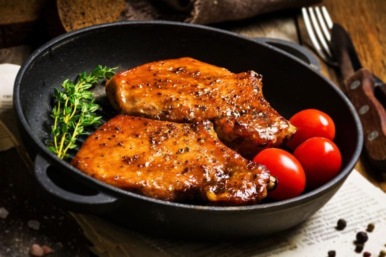 Baked pork chops in sweet honey glaze, served in grill iron skillet with fresh thyme, rye bread and cherry tomatoes, close up, At What Temperature To Bake Pork Chops?