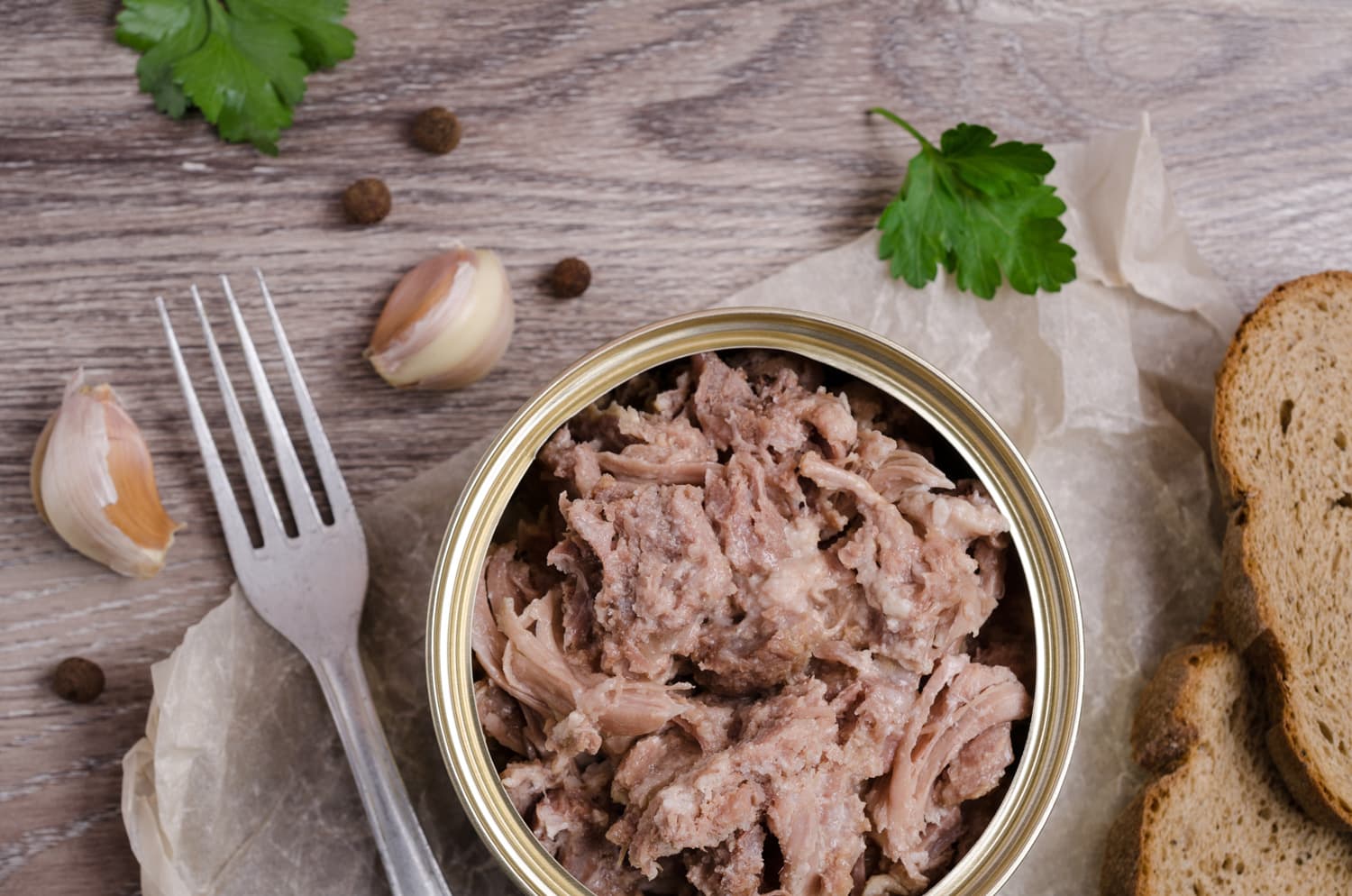 Canned meat fillet in a metal can on a wooden background. Selective focus.