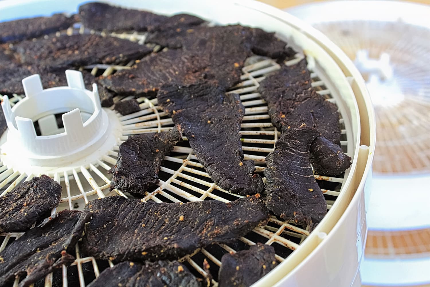 Closeup of dried spiced deer jerky slices on a dehydrator.