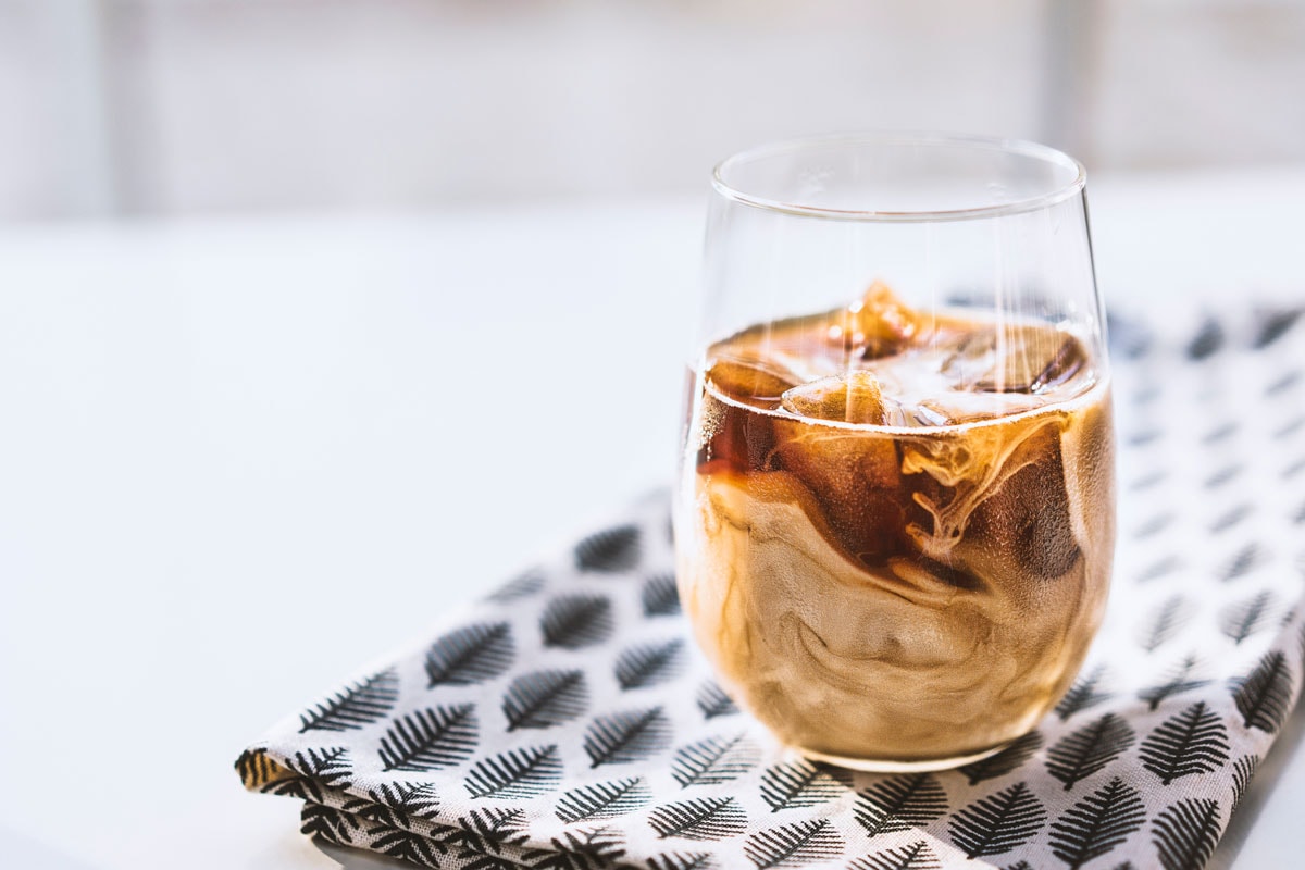 Coffee ice cubes with milk in glass cup on leaf patterned tea towel