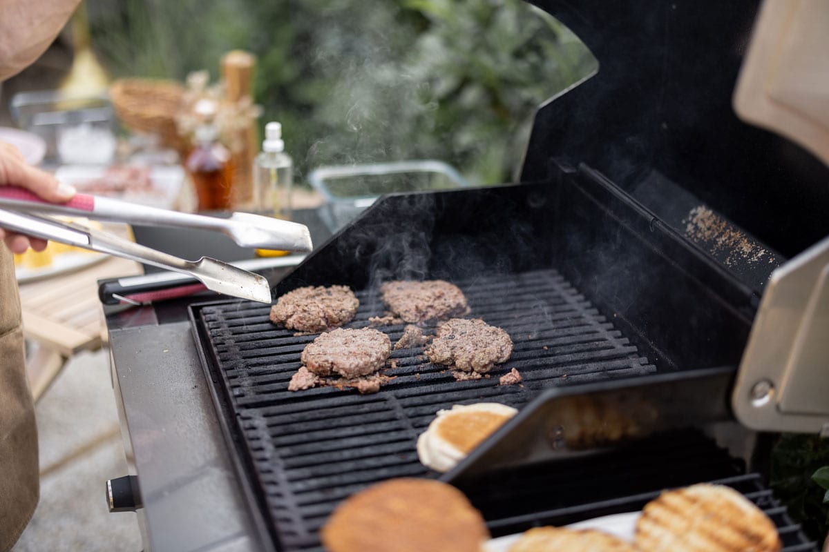 Friends grilling meat and buns for a burger on a gas grill outdoors