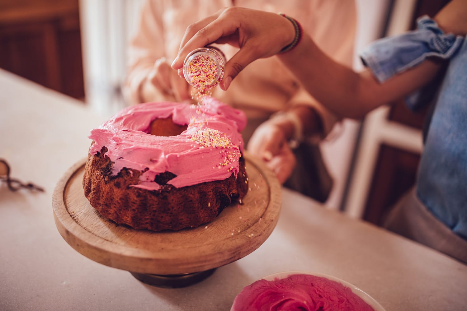 Girl decorating homemade cake with pink icing and colorful sprinkles while baking at home