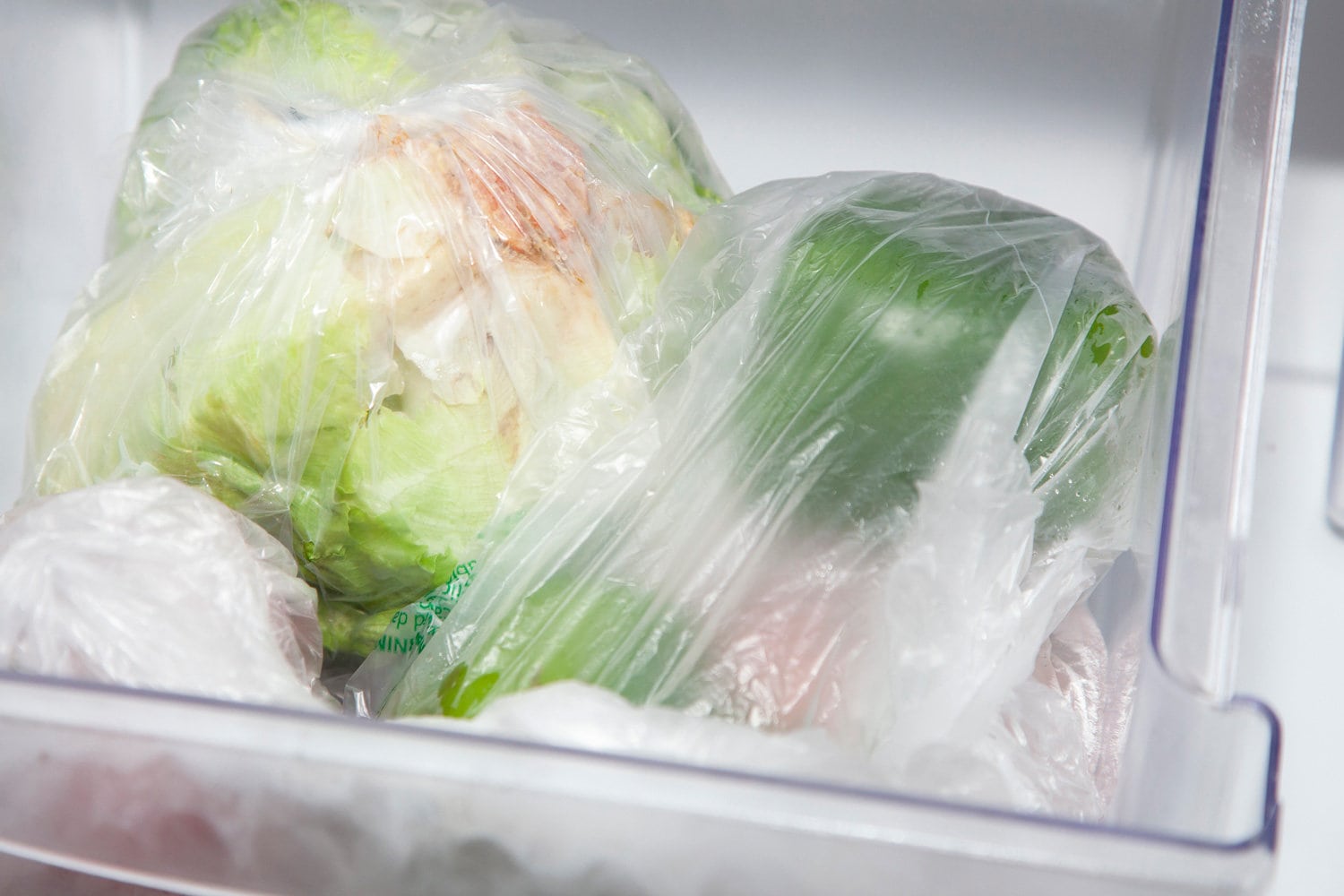 Head of iceberg lettuce, onion, tomato, and bell peppers in vegetable bags in the crisper bin