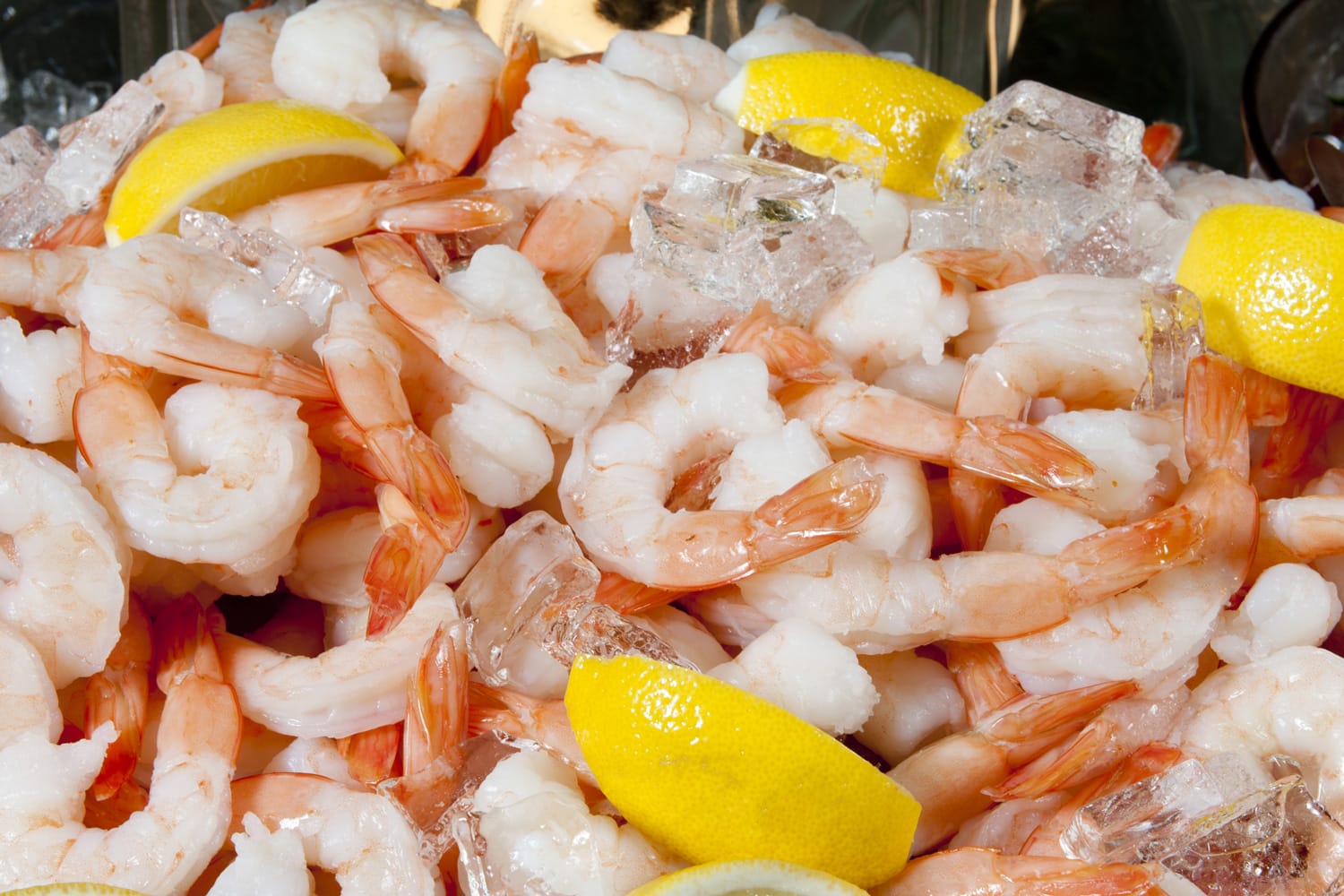 Large pile of fresh shrimp on ice, garnished with sliced lemons